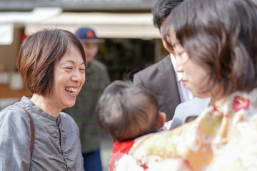 Obraz premium A woman is smiling at a baby while another woman looks on. The baby is being held by a man