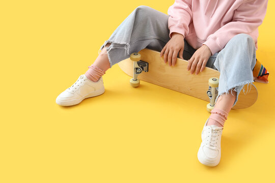 Young woman with skateboard sitting on yellow background - Powered by Adobe