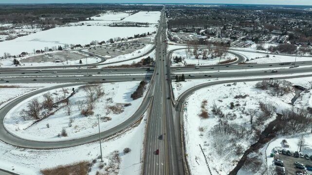 Winter Traffic Hyperlapse on Cloverleaf Interchange. A diagonal aerial hyperlapse shows daily traffic on a busy highway ramp system in winter, with snow covering the ground.