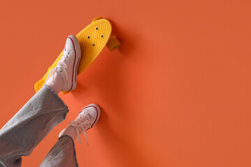 Female legs with skateboard on orange background