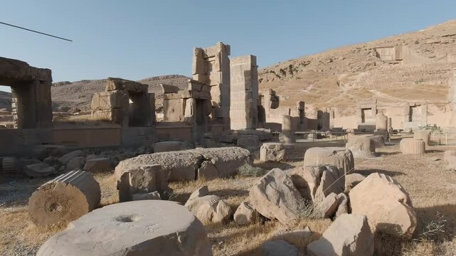 Smooth tracking shot across Persepolis ruins, weaving among toppled column drums and ancient gateways under warm afternoon light&mdash;Achaemenid archaeology with a vast desert backdrop.
