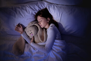 Cute girl sleeping with bunny toy in bedroom at night
