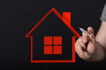 Conceptual image of a hand drawing a red house outline on a dark backdrop, symbolizing home ownership, real estate, and design.