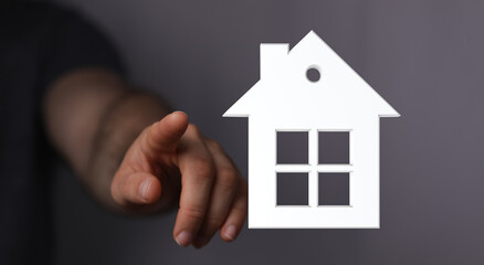 Hand pointing at a house symbol. Concept of choosing a new home, real estate purchase or investment, home ownership. Home icon concept.