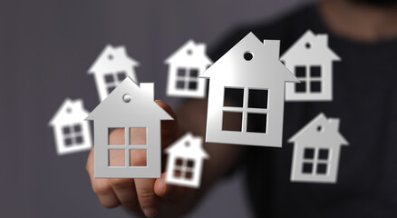 A hand holding several small white house cutouts in the air, showing the concept of real estate and the housing market. Suitable for property in