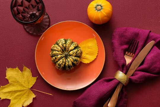 Beautiful table setting with autumn leaves and pumpkins on red background