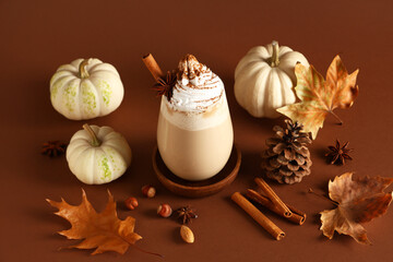 Glass of hot pumpkin latte with whipped cream, cinnamon and hazelnuts on brown background