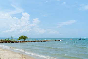 Caribbean beach with rocky jetty, trees and boat in motion, Coveñas coast, Colombia