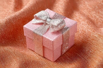 Pink Gift Box with Glitter Bow on Textured Orange Fabric Background