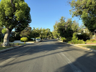 empty residential suburban street (driveways, homes, houses, parked cars, trees, hedges, lawn) beneath a beautiful bright blue sunny summer sky - Los Angeles, California