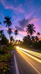 A road through a tropical island is lit by car lights during a vibrant sunset