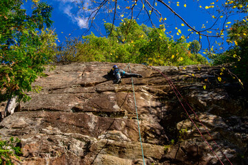 Young woman rock climbing outdoors with top rope belay shot in Calabogie Ontario in fall	room forf text