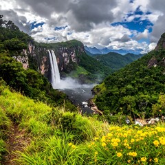 A breathtaking landscape with a powerful waterfall cascading into a serene pool surrounded by lush green hills under a cloudy sky