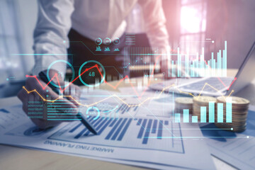 A business professional examines detailed financial data charts and graphs in a modern office,...