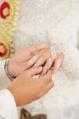 Groom Placing Wedding Ring on Bride's Hand with White Henna and Traditional Attire