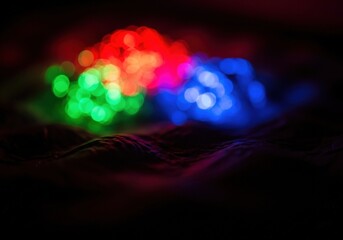 Abstract background of red, green, and blue bokeh lights glowing in the dark on a textured surface.
