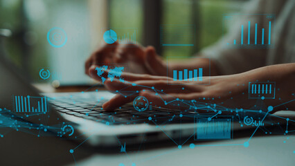 Close-up of hands typing on a laptop keyboard with overlay of digital graphs and data visualizations, representing modern technology and innovative work environments. Xenic