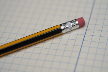 Close up shot of a pencil with an eraser on a graph paper with blue lines and squares