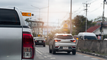 Close up rear side of pickup car silver color. Car is driving in the left lane. And on the right lane there is another car driving with its brake lights on. Road barriers made of large cement.