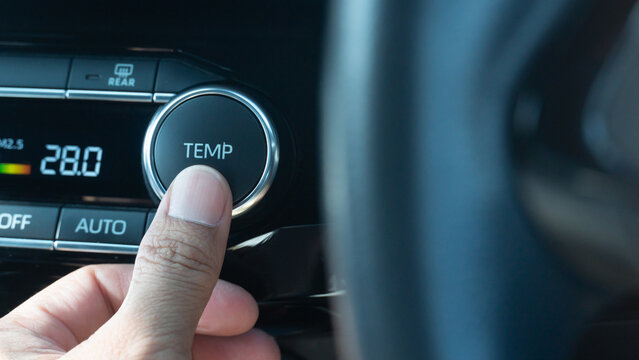 Finger of driving control a Temp button of car. Air conditioner is controlled at 28 degrees Celsius. The front with blurred of car steering wheel.