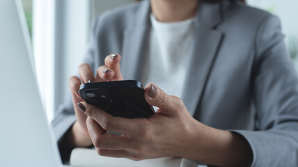 Close up of business woman using smartphone during working on laptop computer at office. Businesswoman using mobile phone, surfing the internet, searching the information at workplace