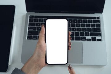 Smartphone white screen mockup, Woman hand holding mobile phone with blank screen while working on laptop at office. Business woman using cell phone, mockup for social media marketing