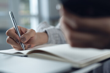 Close up of business woman using smartphone searching the information, writing on notebook, planning new business project during working on laptop computer at home office