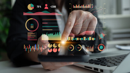 A professional engages with business analytics and data visualization using a smartphone and laptop...