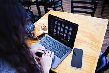 Woman editing photos on a laptop at a wooden cafe table with a c
