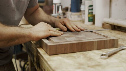 Woodworker marks decorative panel with metal ruler on cluttered bench