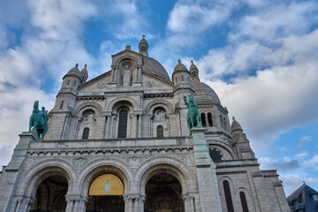 Sacre-Coeur Basilica in Paris with equestrian sculptures and white domes on a partly cloudy day atop Montmartre hill