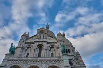 Fototapeta premium Sacre-Coeur Basilica in Paris with equestrian sculptures and white domes on a partly cloudy day atop Montmartre hill