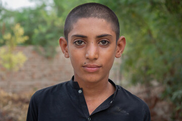 a calm and confident young person with a buzz cut and nose piercing, wearing a black shirt and looking directly at the camera.