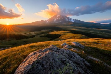 Breathtaking view of a towering mountain peak against a vibrant sunset sky with a rolling meadow in the foreground and rugged terrain in the distance