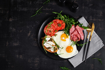 English breakfast. Fried eggs, salami, tomatoes and toast with feta and pesto. Top view.