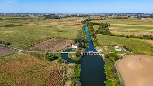 Small hydro station and weir on the Prosna River surrounded by farmland seen from drone showing rural landscape and river meanders in central Poland