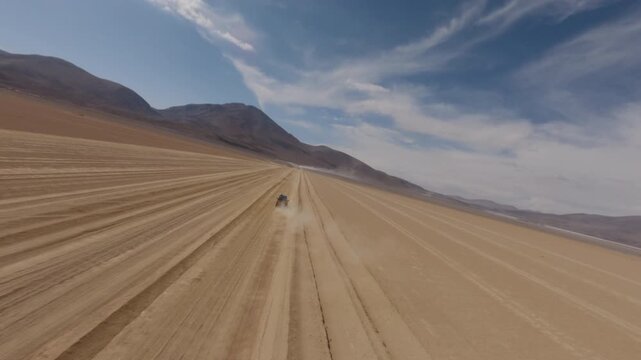 FPV drone shot of a 4x4 driving fast along a gravel road in the Bolivian Altiplano during daylight surrounded by desert terrain and distant mountains in a cinematic scene