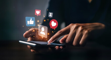 A persons hand interacting with a smartphone, with social media icons such as a thumbs up and a heart emerging from the device, symbolizing digital interaction and online community