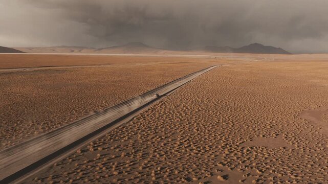Aerial shot at sunset of a 4x4 driving along a gravel road across the vast highlands of the Bolivian Altiplano surrounded by dramatic skies and desert landscapes