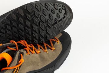 Beige hiking boots with colorful orange laces on a white background. One shoe upside down presenting grippy sole. Photo taken under artificial lighting.