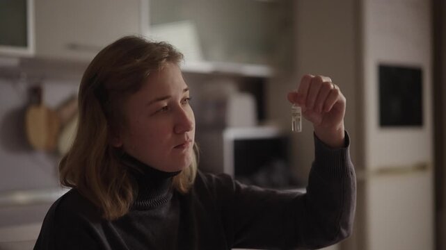 Close-up face of young woman with cerebral palsy holding glass vial, examining liquid inside, contemplating personal health, medication and implications of treatment for medical conditions at home.