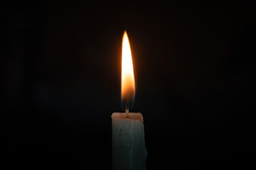 A single white candle burning brightly in the dark, symbolizing hope, peace, and solitude with a soft warm flame against a black background, in landscape