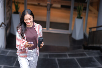 Young woman walking downstairs using smartphone holding coffee