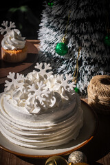 White buttercream cake decorated with snowflake toppers in a cozy Christmas and Happy New Year still life setting. The festive cake is placed on a rustic wooden table with warm light.