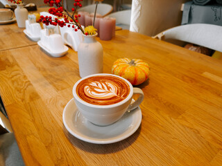 Warm coffee cup with latte art on a wooden table decorated for autumn