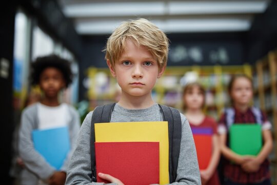 Upset Caucasian boy clutching notebooks surrounded by diverse classmates Themes of education and inclusivity in an elementary setting