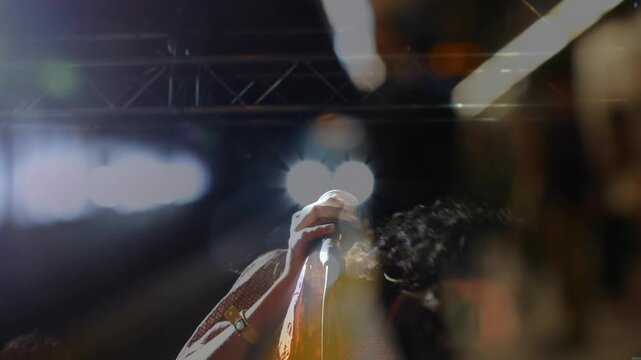 Spotlight revealing singer on stage gripping mic singing music to engage crowd under stage lights