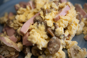 Appetizing close-up of fluffy scrambled eggs with savory ham and fresh mushrooms. A perfect concept for a hearty breakfast or brunch, showcasing a delicious and high-protein meal.