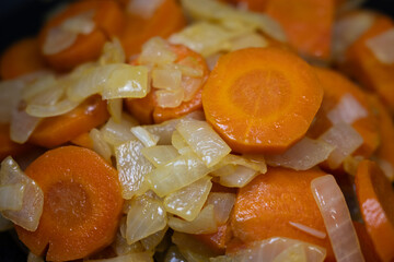 Close-up of fresh sliced carrots and chopped onions sautéing in a pan. Vibrant, healthy vegetables for cooking concepts, meal prep, and delicious homemade food.