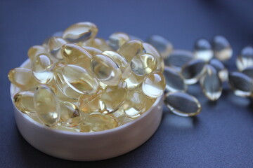 A pile of transparent omega capsules with golden liquidin a white container cap.